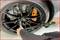 A person is tightening the wheel nuts with a torque wrench on a black car with an orange brake calliper.