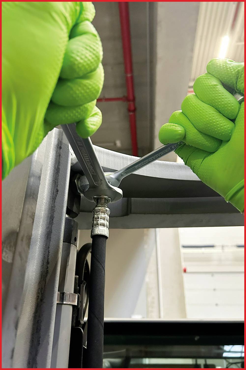 A person wearing green gloves is repairing a metal device with a spanner, demonstrating technical work or maintenance.