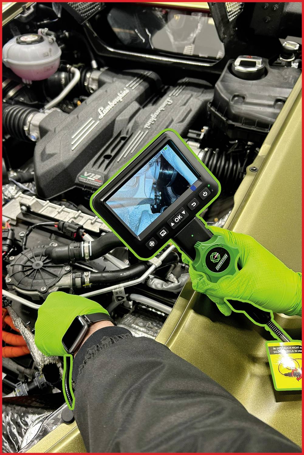 A person is examining the engine compartment of a vehicle using a camera on a flexible rod. The camera displays an enlarged image on a screen.