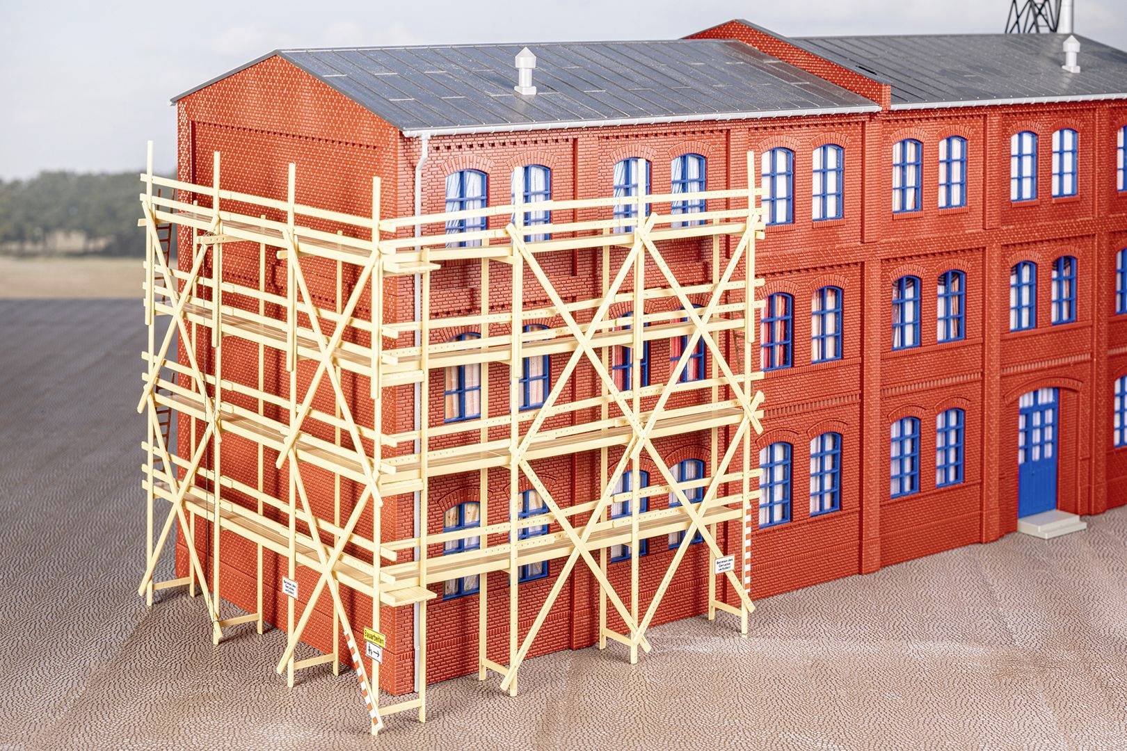 Brick building with blue-painted windows. In the foreground, a wooden scaffolding is erected, extending across multiple storeys.