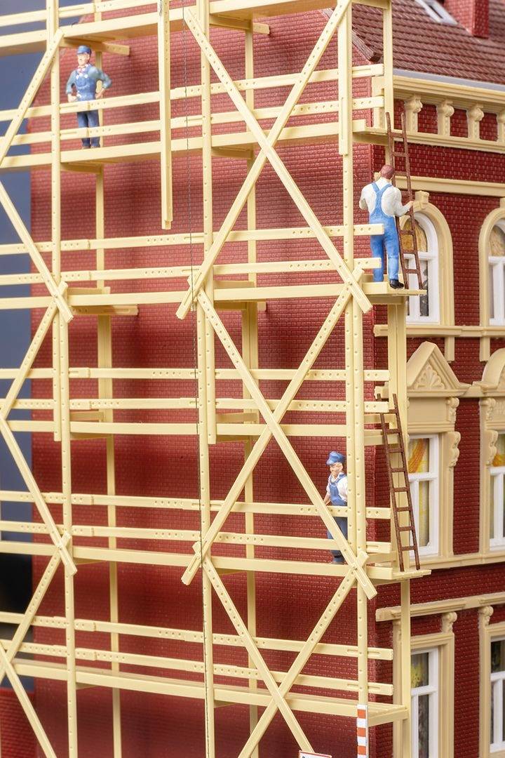 Three workers on a scaffolding at a brick building. One is standing at the top, the others are lower down. They are wearing safety helmets.