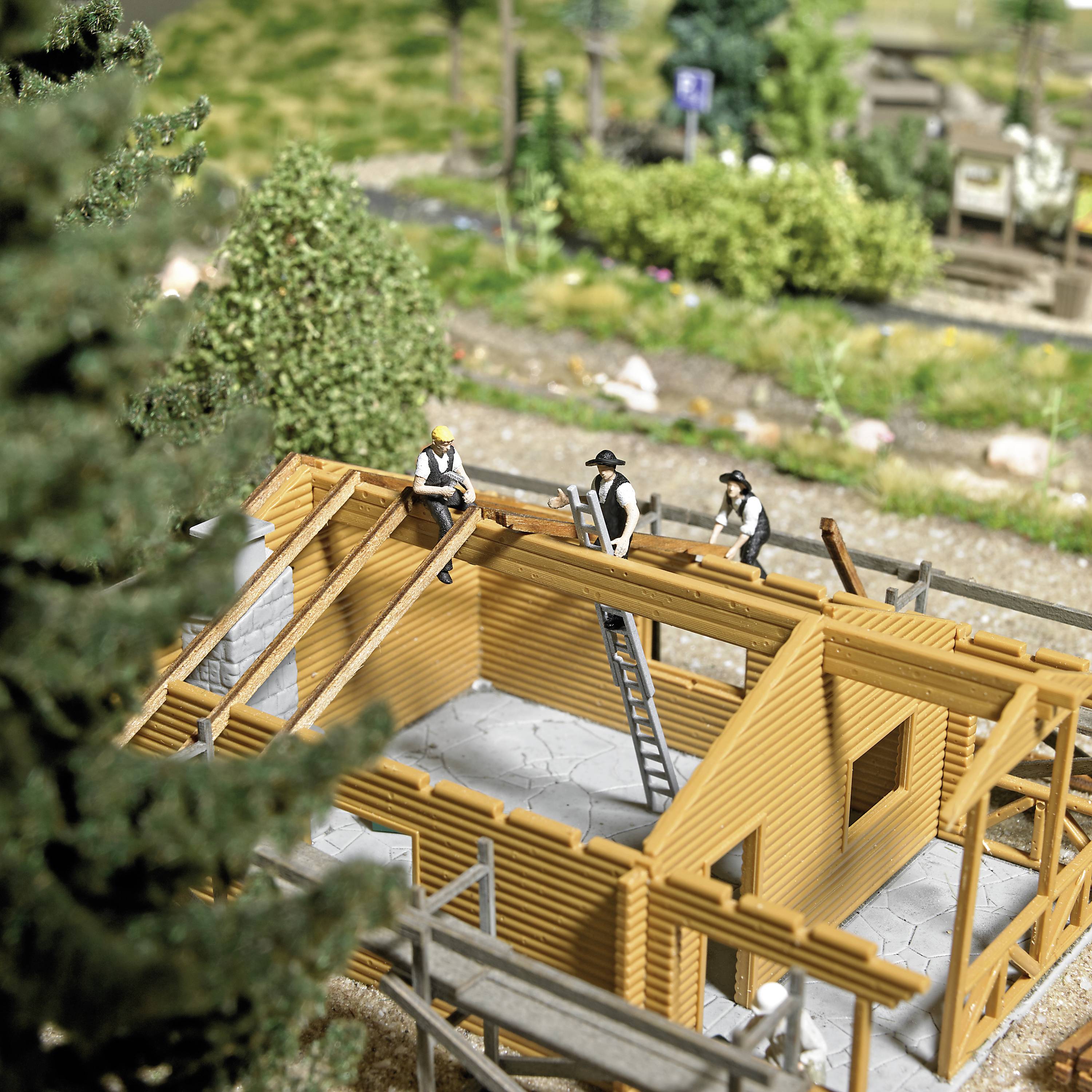 Miniature scene with craftsmen on a half-finished wooden house, surrounded by trees.