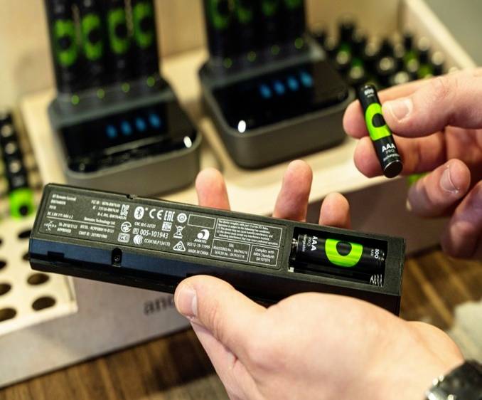 A person is holding a remote control powered by rechargeable AA batteries in front of a battery charger.