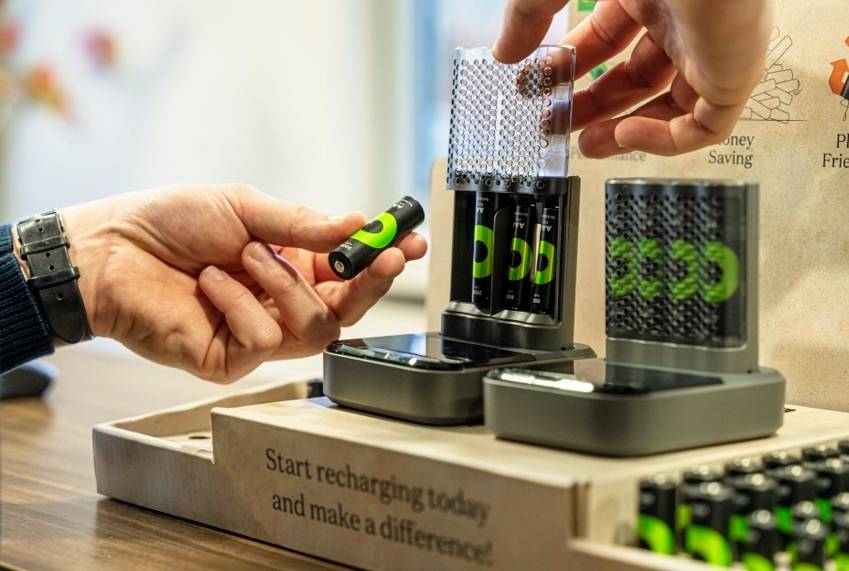 A person is removing a rechargeable battery from a charging station. Background note: 'Start recharging today and make a difference'.