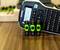 A label printer and three rechargeable AA batteries on a wooden table. The printer displays a screen and a keyboard.