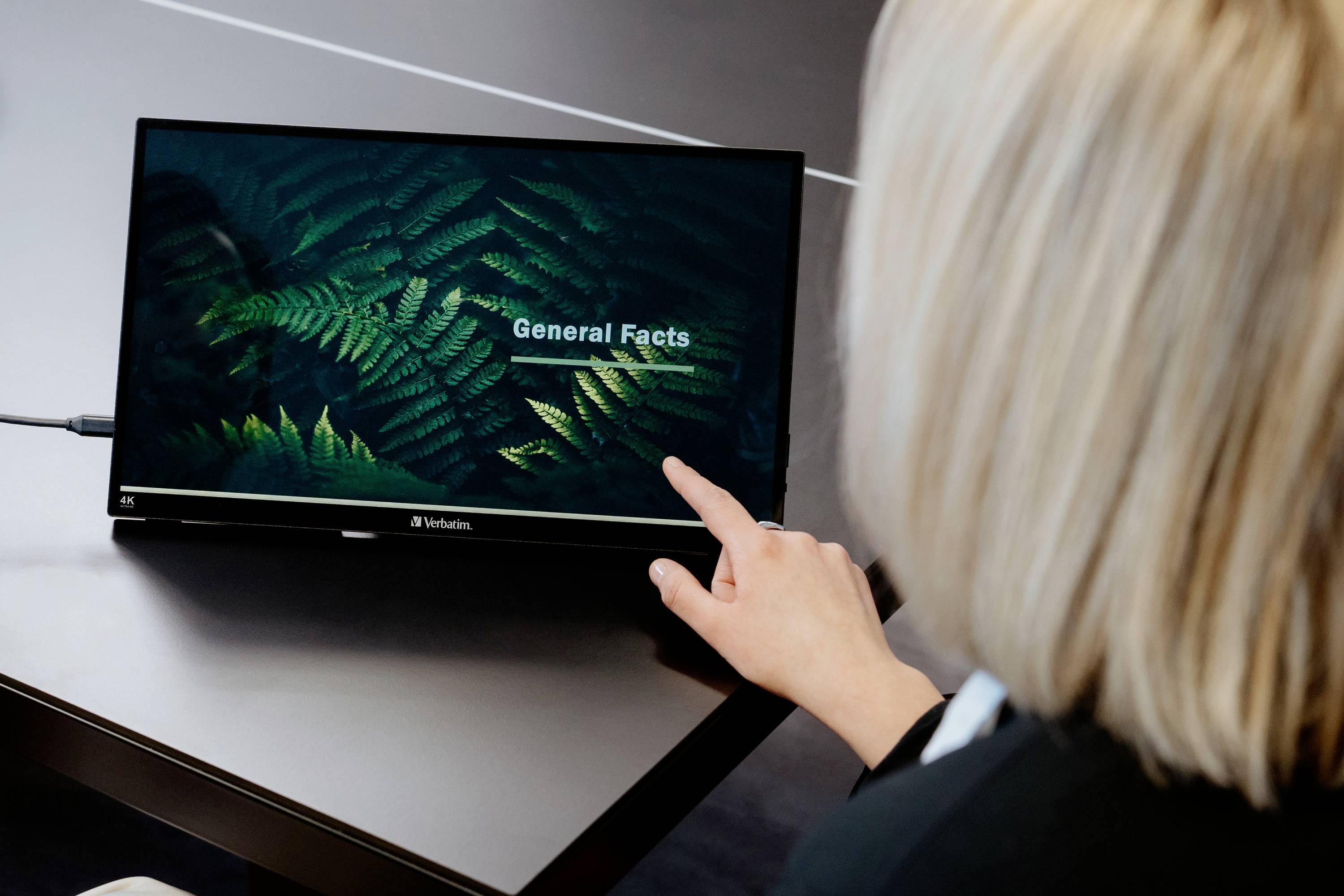 A person is pointing at a screen displaying 'General Facts' against a background of fern leaves.