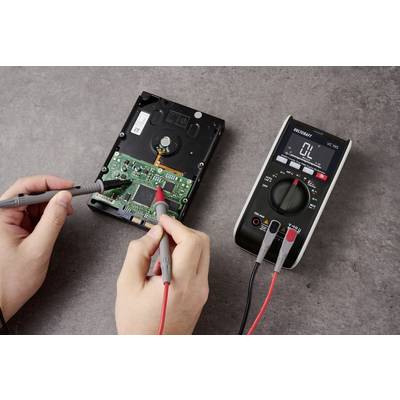 A person uses a multimeter to test an open hard drive, measuring electrical values on the circuit board.