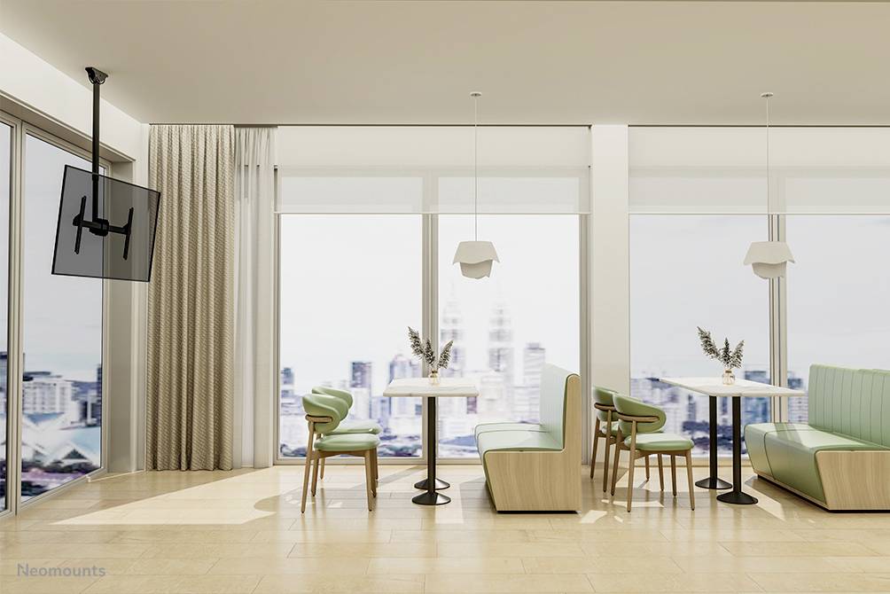 Bright café with large windows, green benches and two tables with chairs. City view visible through the windows in the background.