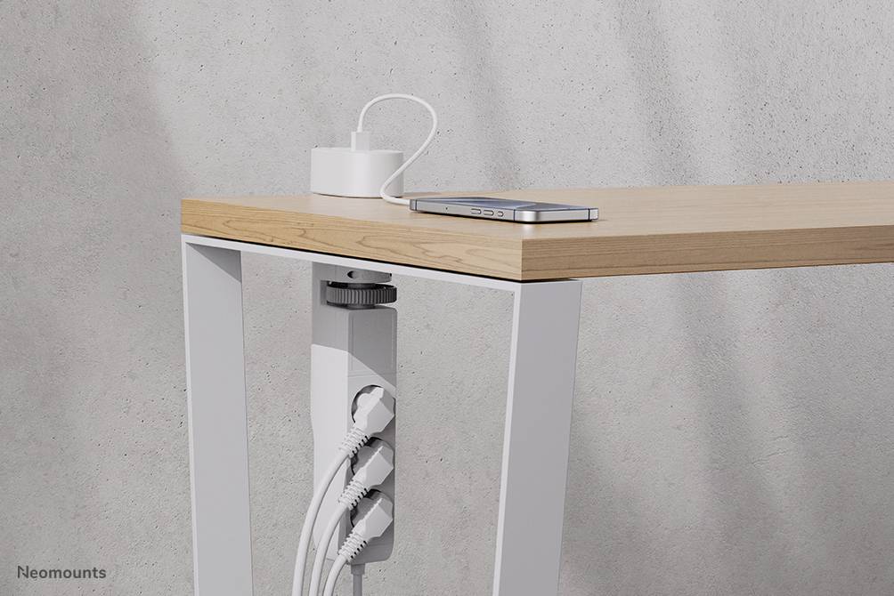 Mobile phone on a wooden table with a white table leg. Several cables are neatly attached to the table leg.