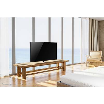 A modern room with large windows shows a television on a wooden table, with a view of the sea. An armchair stands beside it.