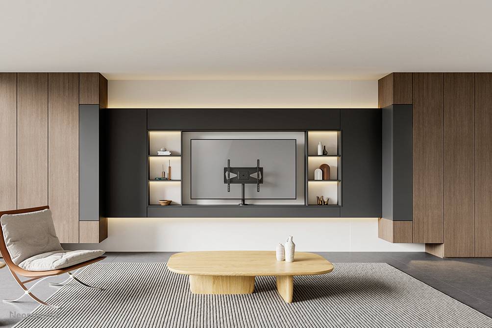 Modern living space with wall shelving, a large flat-screen television mounted on the wall, a lounge armchair and a wooden table on a carpet.
