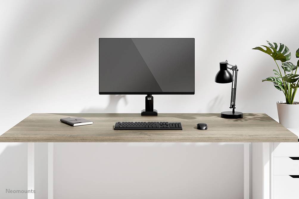 A minimalist desk with a monitor, keyboard, mouse, lamp, notebook and a plant.