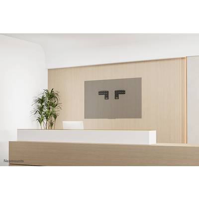 A modern wooden reception desk with a plant pot to the left and a wall-mounted screen holder on the wall behind it.