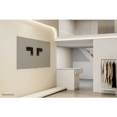 Wall with TV mount in a modern, minimalist living space. To the right, a clothing stand with garments, with a white reception desk in the background.