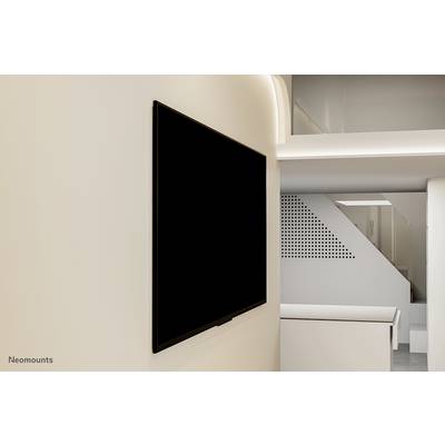 On a bright wall hangs a large, black flat-screen display. Modern architectural details are visible in the background.