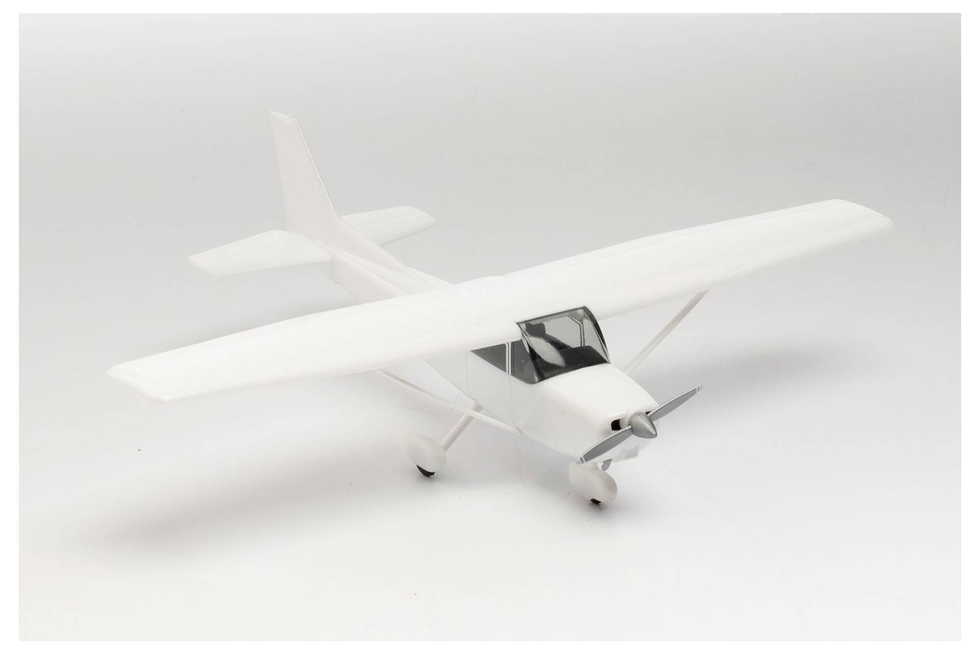 A white model airplane sits on a white background. It shows a single-engine propeller aircraft with two wings.