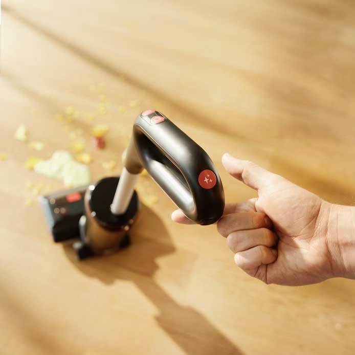 A cordless vacuum cleaner sucks dirt from a wooden floor; a hand holds the handle for easy cleaning.