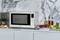 A microwave sits on a marble worktop, surrounded by ingredients such as tomatoes, cheese, broccoli, and olive oil bottles.