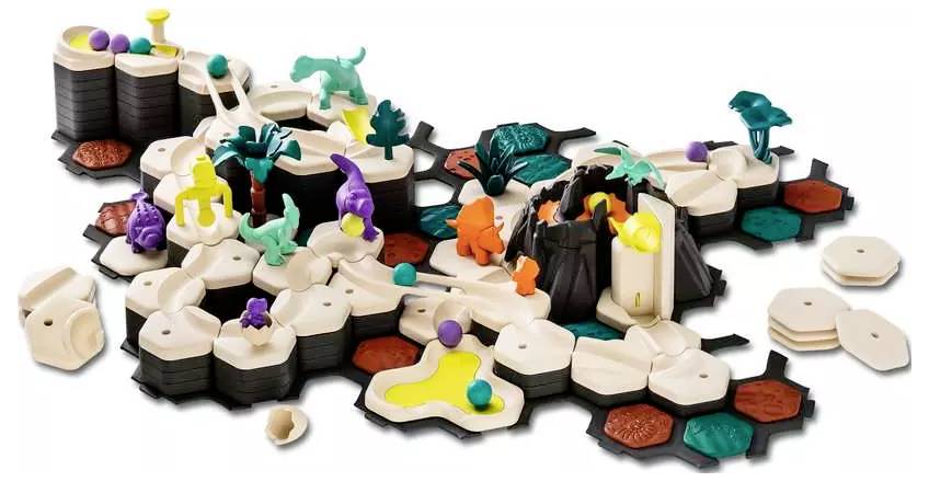 A board game setup featuring dinosaur figures, a volcano, hexagonal tiles, and colorful marbles representing lava flows and terrain.