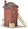 A small red brick building with a chimney and roof. A wooden staircase leads up from the side. A small shed stands beside it.