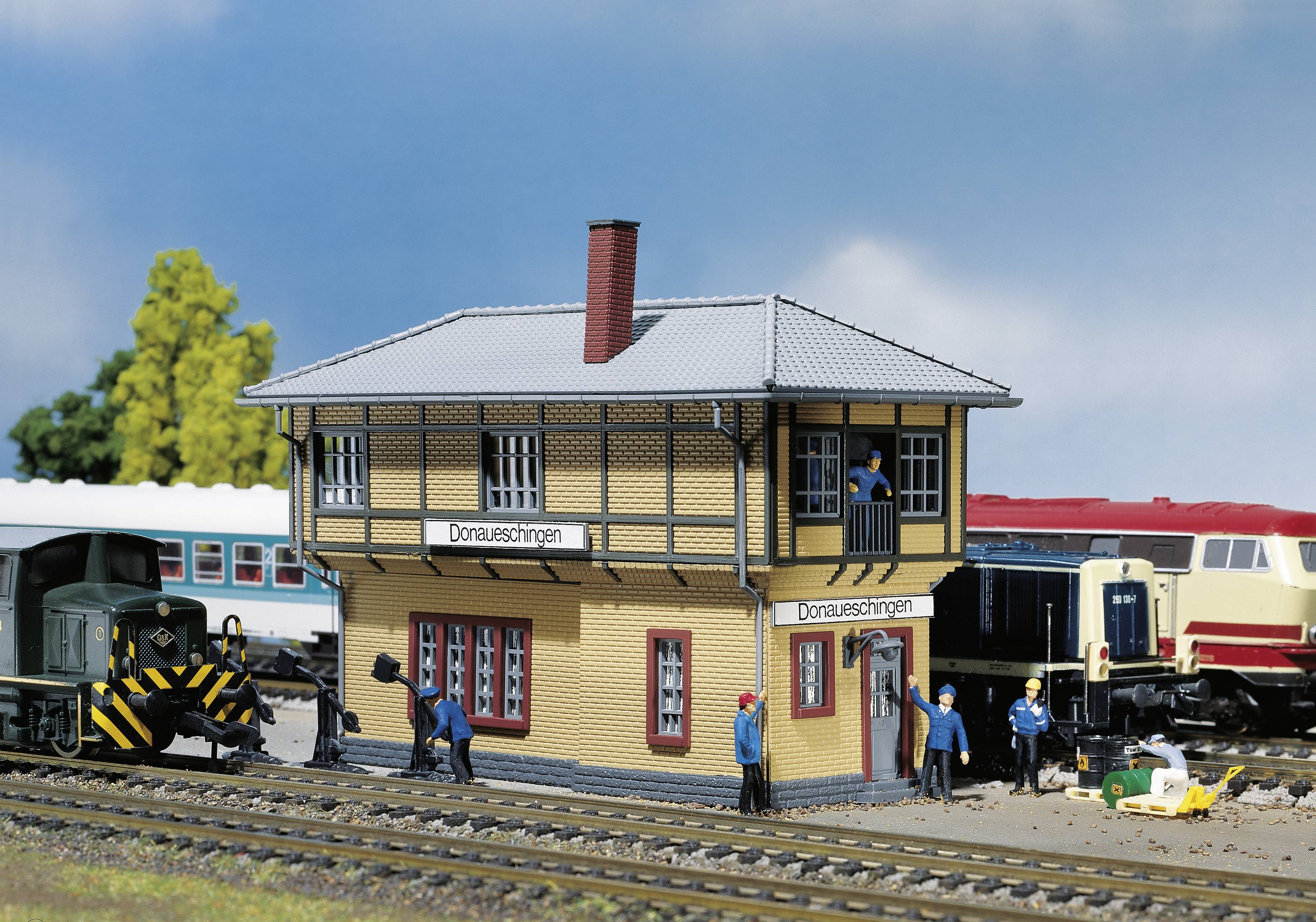 'Model railway scene with station building, two trains and figures; depicts a station environment with activities and details in miniature form.'