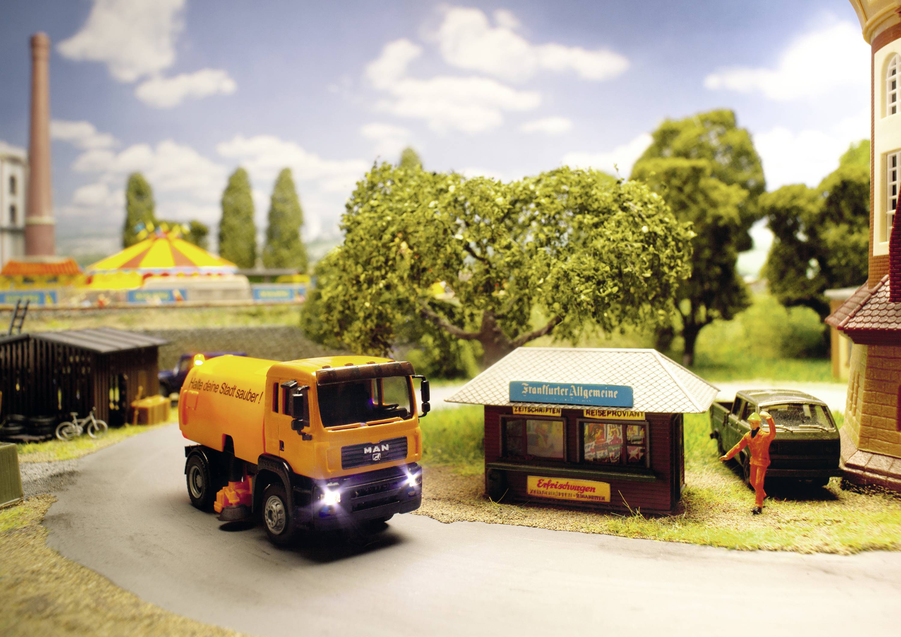 A model of a city scene with an orange refuse lorry on a street, a newsagent's shop and a parked car beside trees and buildings.