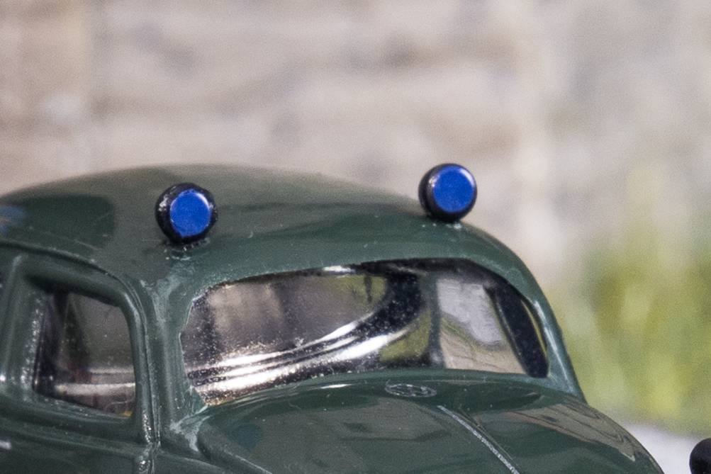 Close-up of a dark green toy car with two blue lights on its roof against a blurred background.