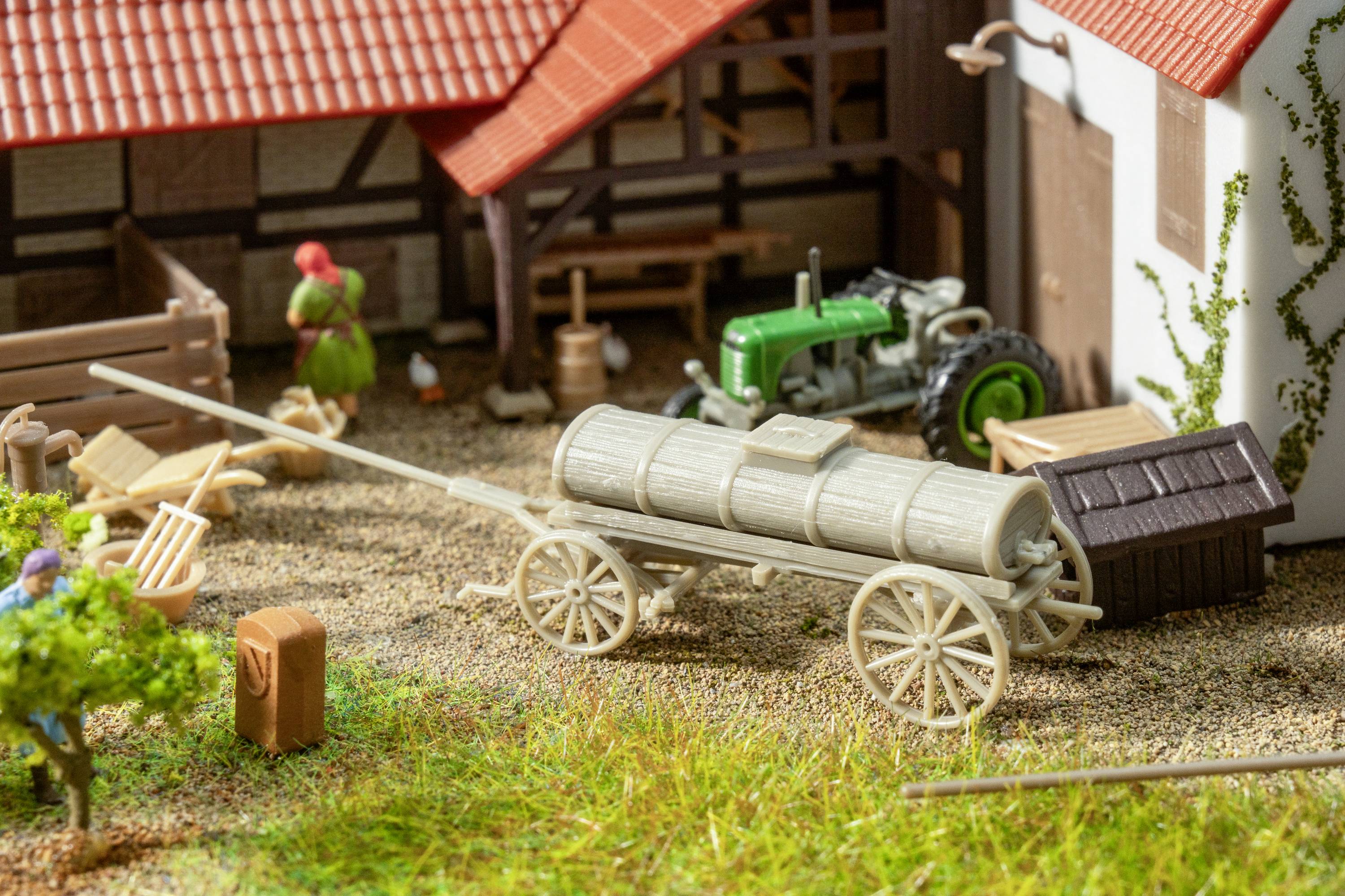 A model farm with agricultural buildings and a tractor. In the foreground, a wooden barrel stands on a wagon.