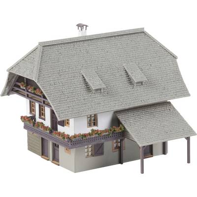 A miniature model of a traditional farmhouse with a grey slate roof, balcony, and window boxes filled with red flowers.