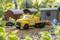 Yellow recovery vehicle on a modelled gravel road. Miniature buildings and plants in the background. A model maker is working on details.
