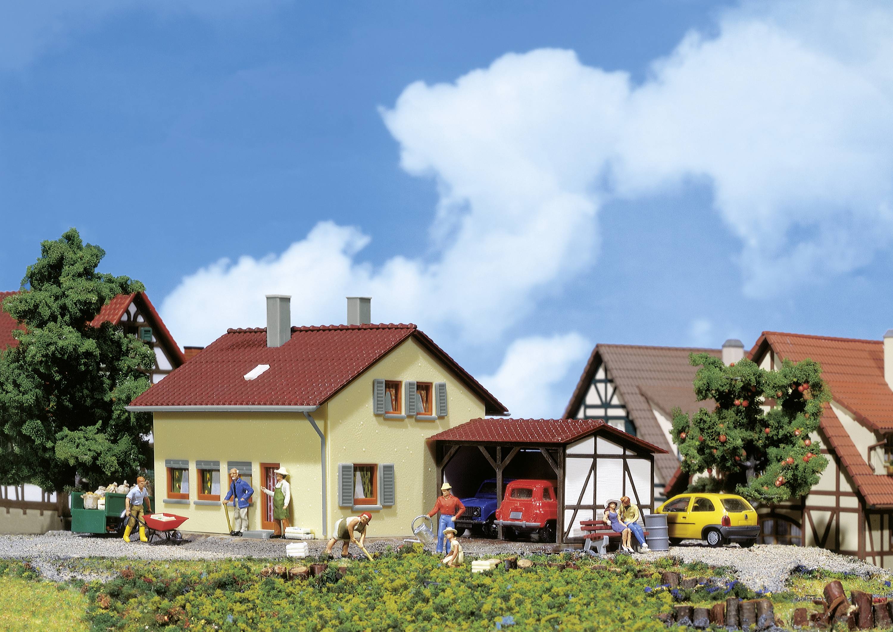 A picturesque village with half-timbered houses. In the foreground, people are working in the garden, with a red car parked in the driveway.