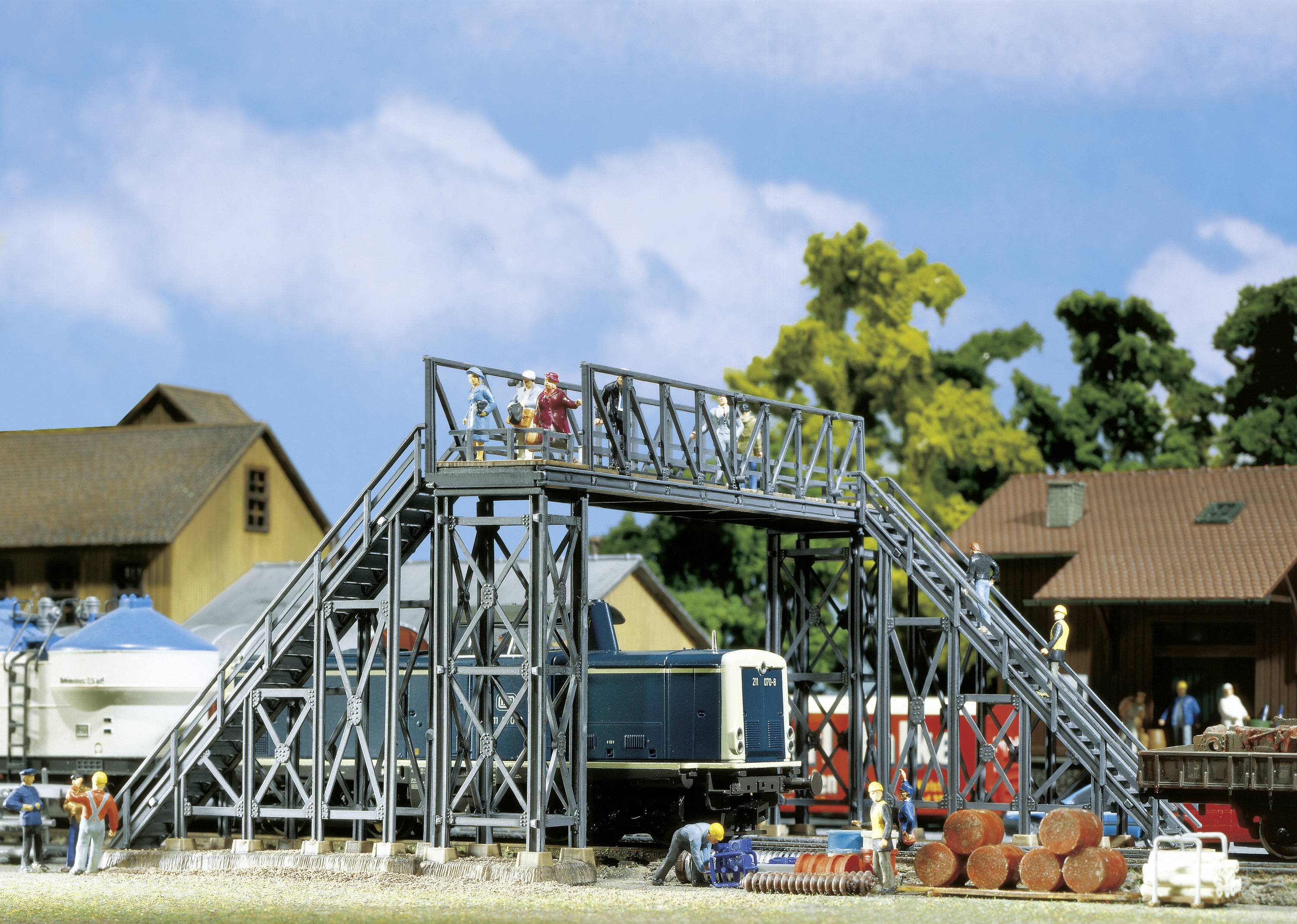 A miniature scene depicts an industrial site with a railway wagon, a bridge with people, and a background of trees and buildings.