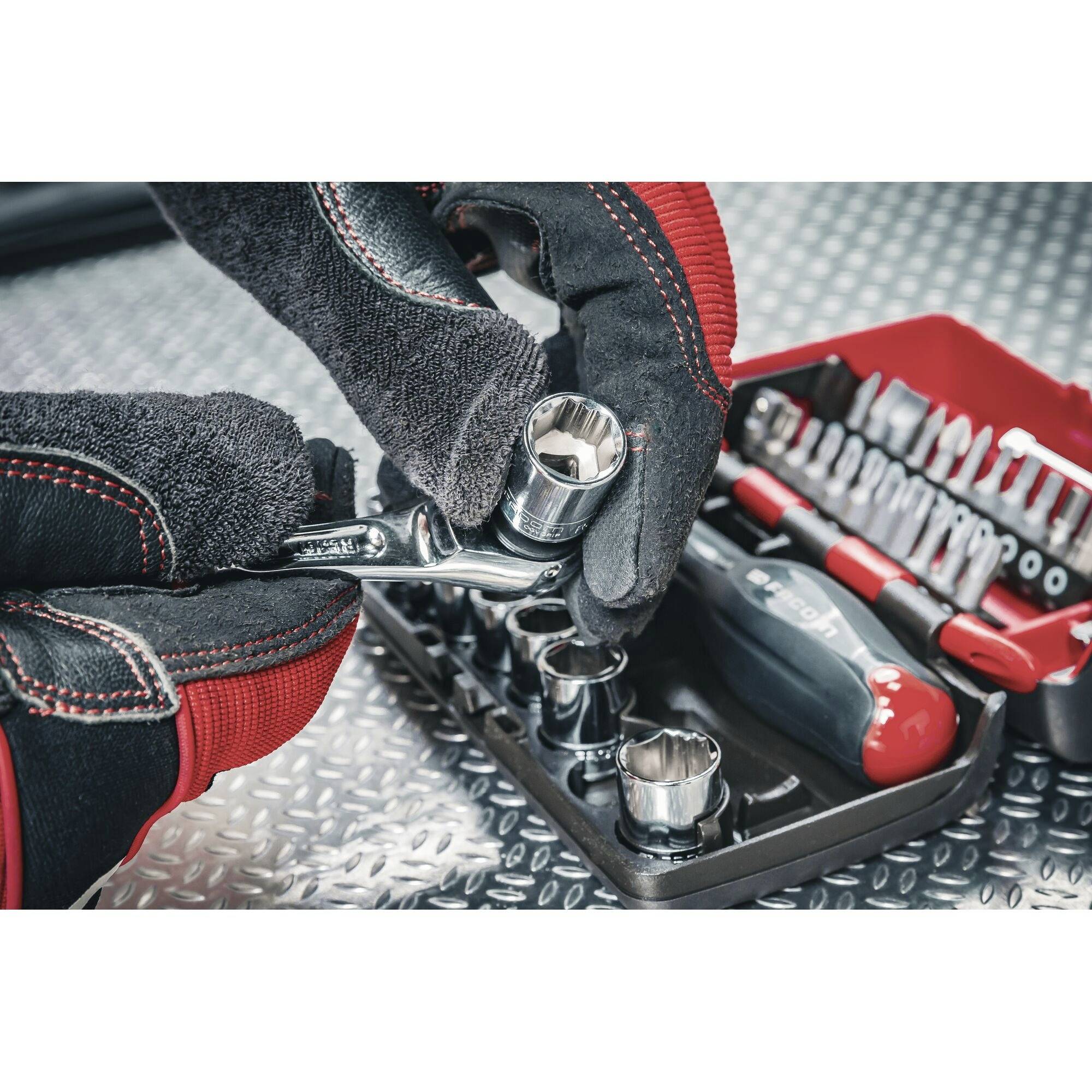 A person is wearing gloves and holding a ratchet with a socket. An open toolbox lies in the background.