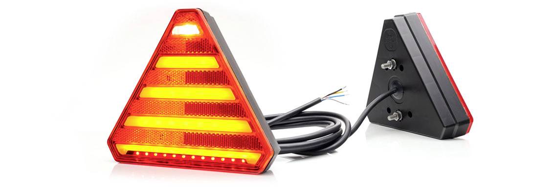 On the left of the image: A triangular, red rear light, shining brightly. On the right: Rear view with cables and mounting points. Usage: Trailer.