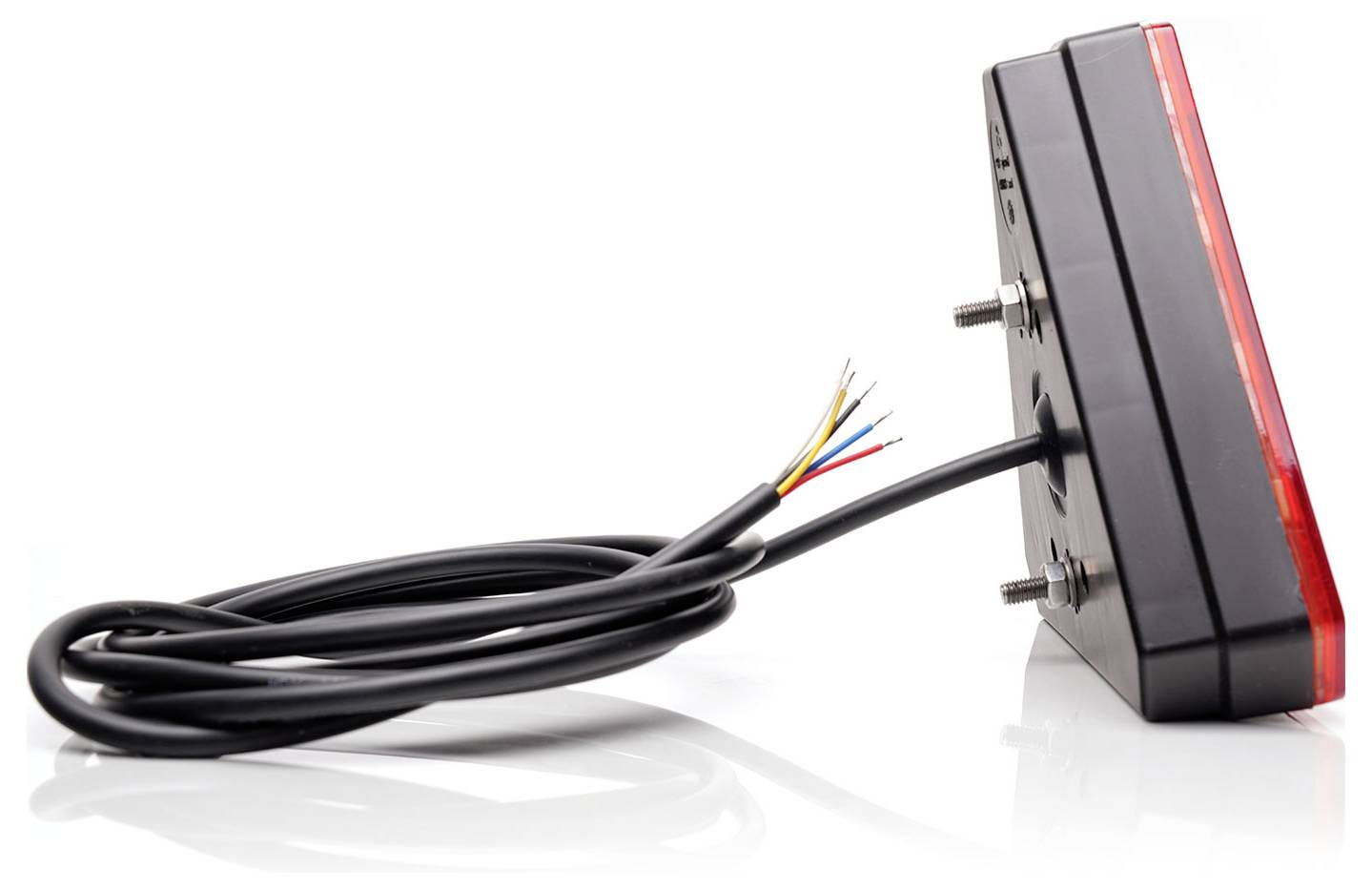 A rectangular rear light with a red lens cover and exposed cables. It has two mounting screws and is placed on a reflective surface.