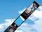 Packaging of a stunt kite in blue with a viewing window, against a blue sky with clouds. Product details and brand visible.
