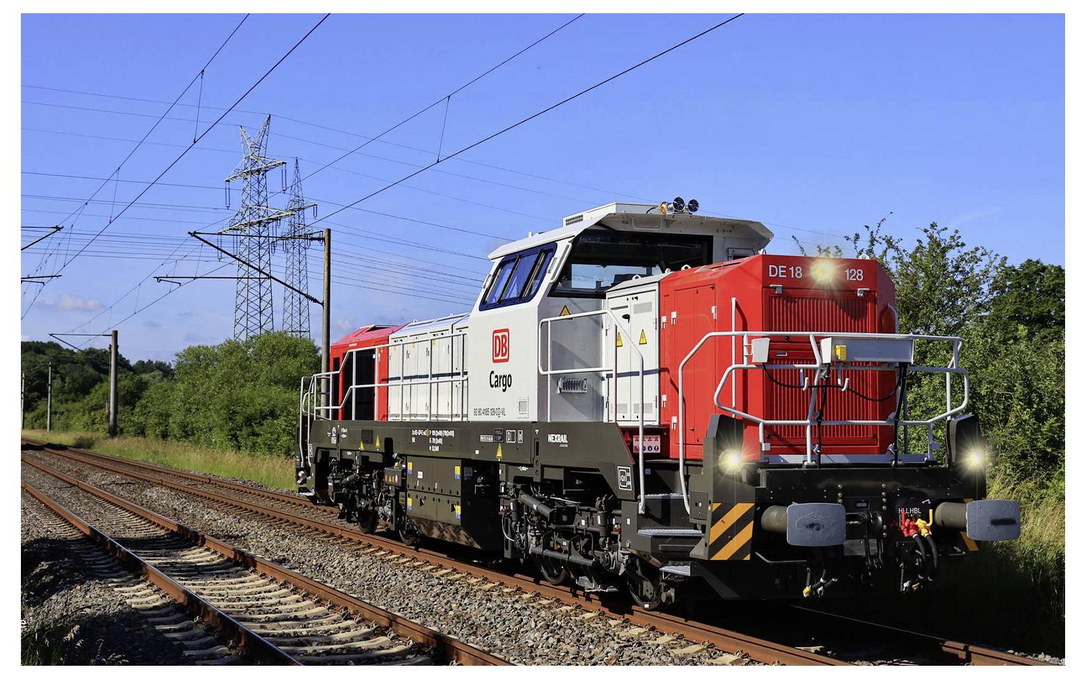 A red freight train from DB Cargo travels during the day along a railway track through a rural landscape, surrounded by vegetation and electricity pylons.