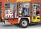 A fire engine shows open storage compartments with tools, hoses, cones, and a vacuum cleaner, ready for deployment.