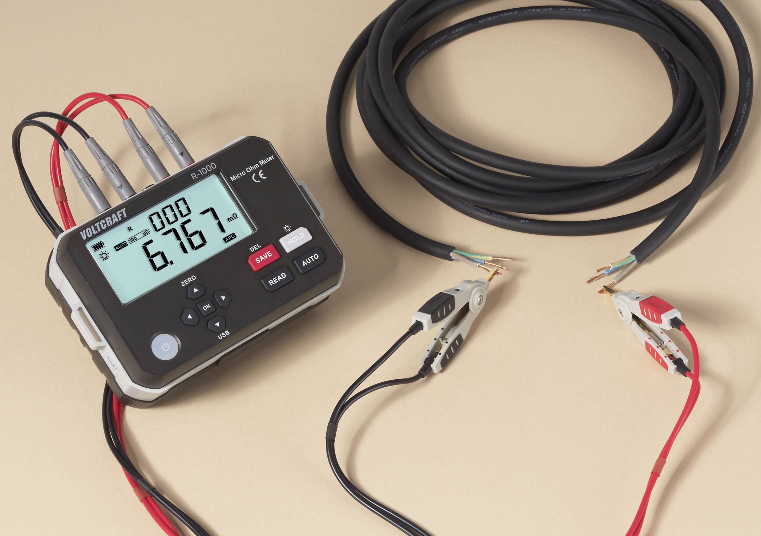 A digital multimeter displaying '6.167' connected to cables with alligator clips. The device has several buttons and a digital screen.