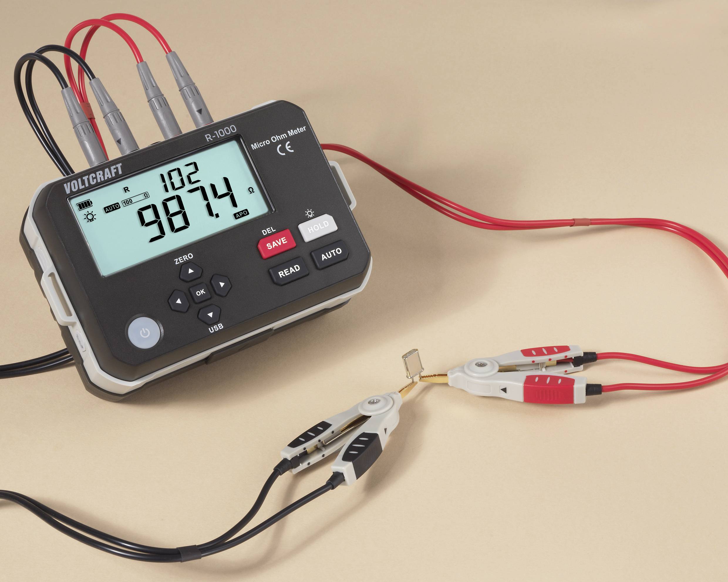 A digital voltmeter with red and black leads displays '98.74'. The leads are connected to a small resistor.