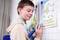 A boy is using an electronic pen on an illustrated board with animal pictures and text. He is concentrating on his task.