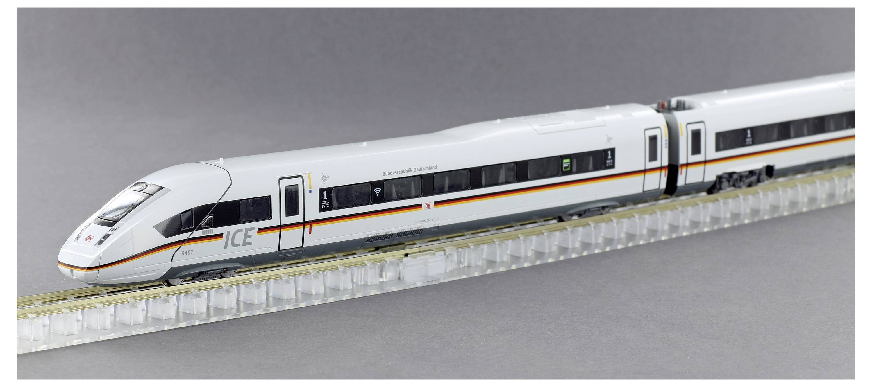 A model of a white ICE train with red stripes travels over a railway track. The train has several cars.