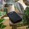 A black garden tool with the 'Fiskars' logo on a wooden table, surrounded by various tropical plants in pots.