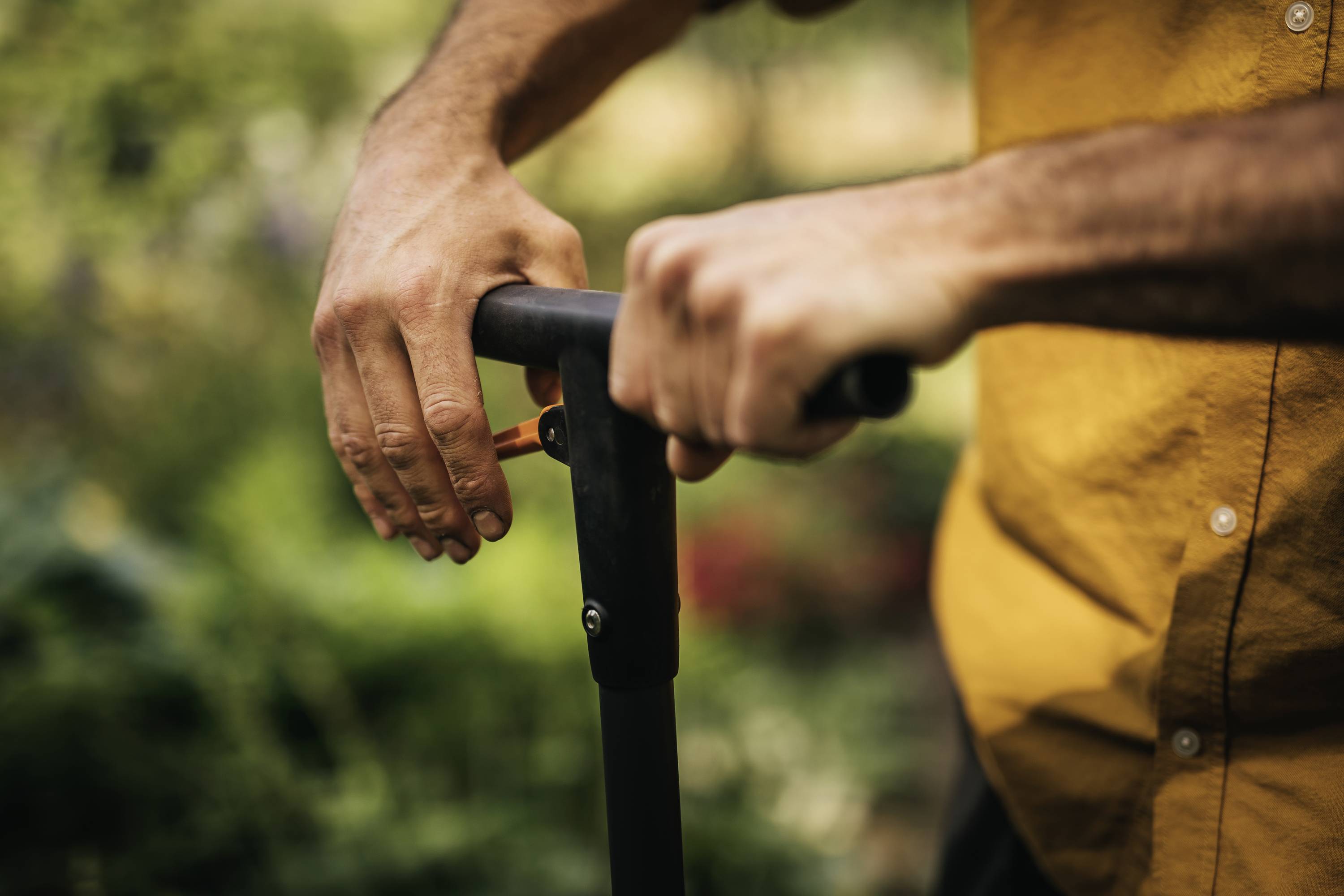 A person is holding the black handlebar of a scooter or bicycle outdoors. The person is wearing a yellow shirt.