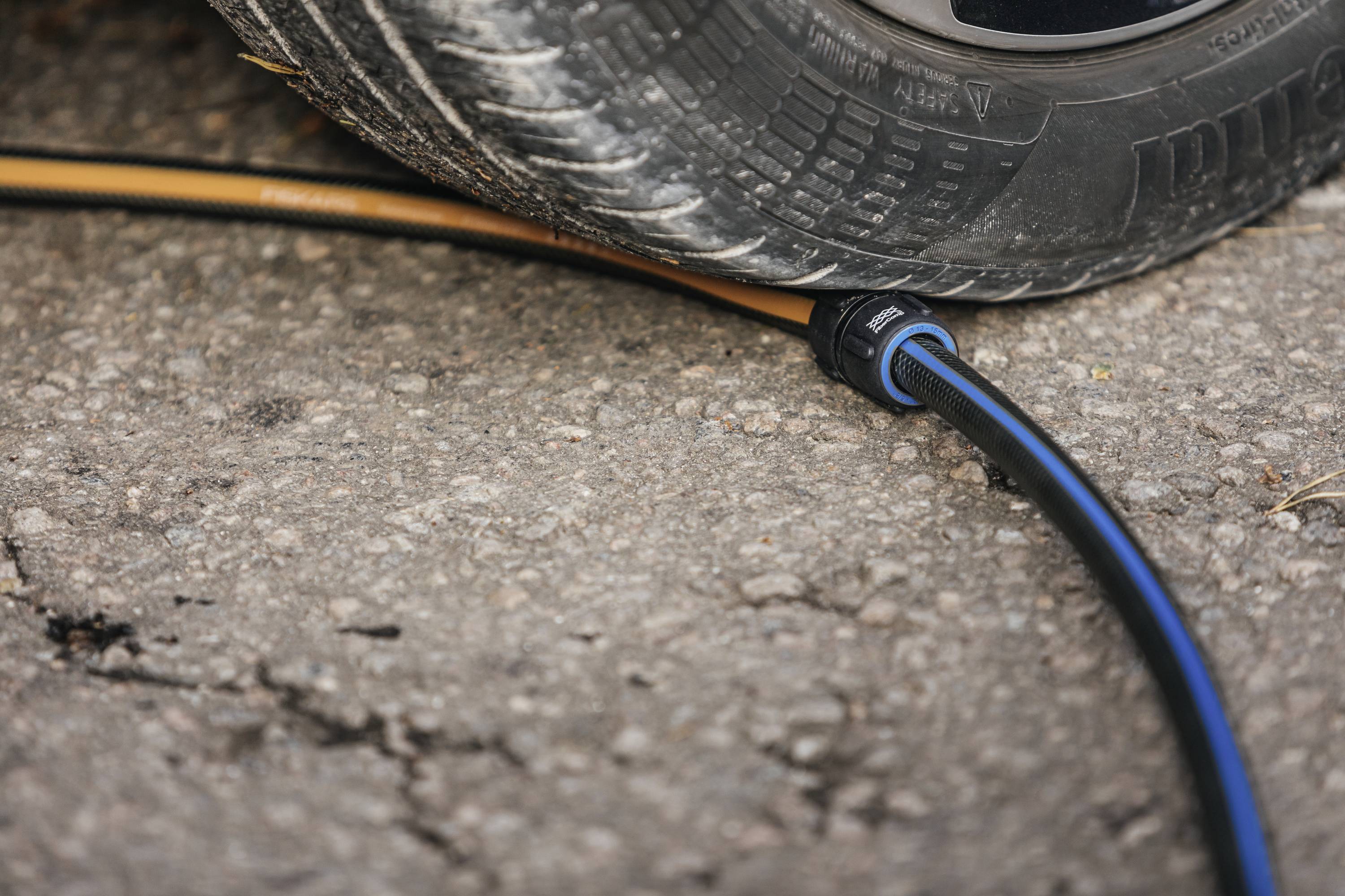 A car tyre is resting on a blue and black cable on an asphalted road, pinching the cable underneath.
