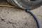A car tyre is resting on a blue and black cable on an asphalted road, pinching the cable underneath.