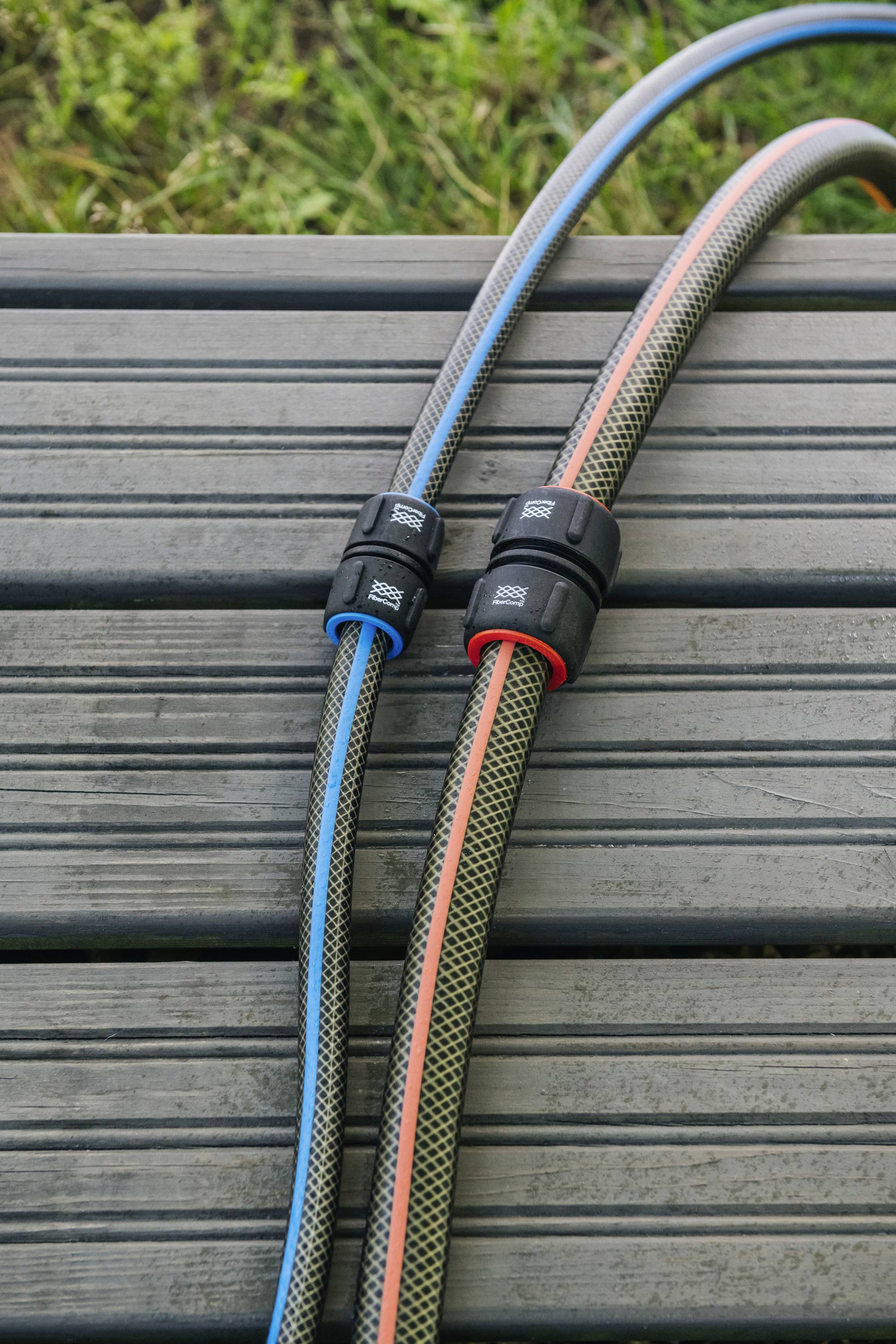 Two interconnected garden hoses on a wooden bench, one with a blue stripe, the other with a red stripe, against a green background.
