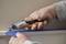 A person is cutting blue adhesive tape at the edge of a white wall panel using an orange-grey utility knife.