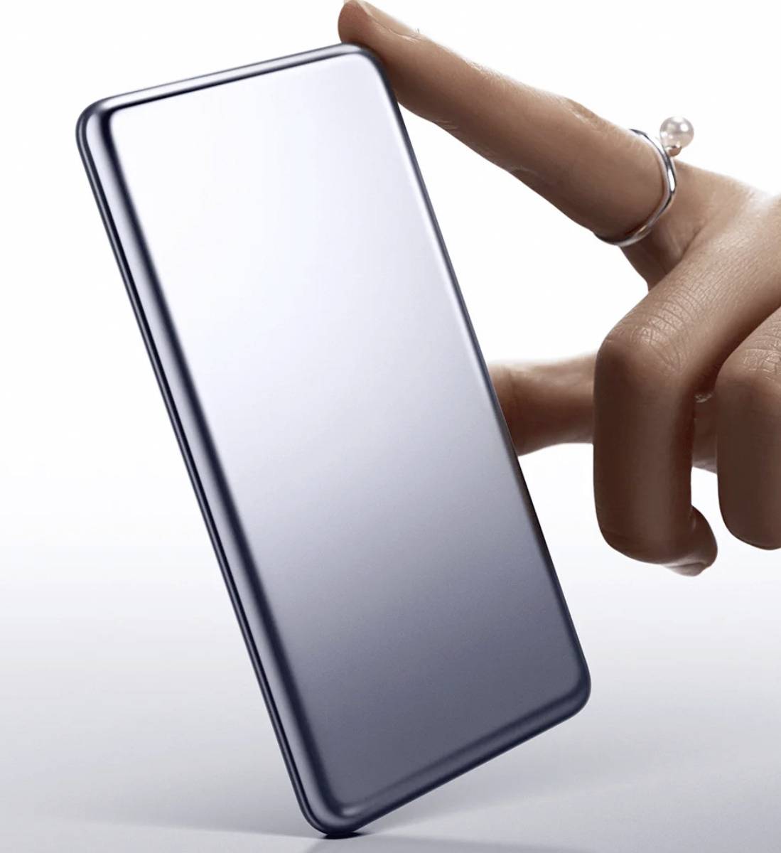 A hand with a ring holds a sleek, modern smartphone, emphasizing its thin profile and metallic design.