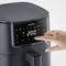 A hand is tapping the control panel of a black air fryer to set the temperature to 200 degrees.